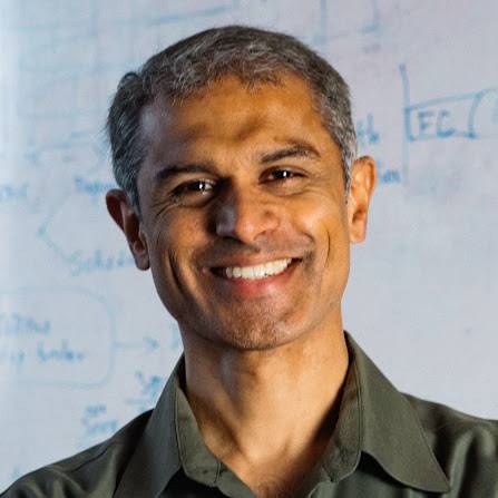 photo of Hari Balakrishnan in front of whiteboard with mathematical figures