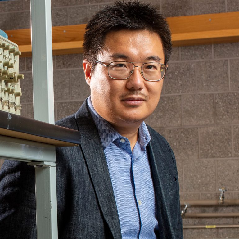 Han a male standing in lab by shelves of equipment
