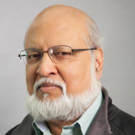 male with glasses and bread in front of grey background wearing collared shirt and jacket