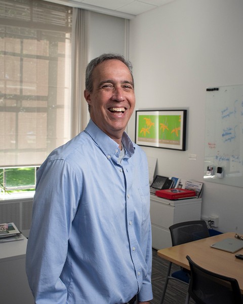 dan huttenlocher standing in his office wearing a blue shirt and smiling