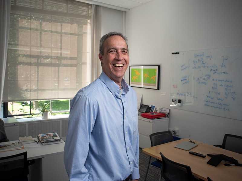 dan huttenlocher standing in his office wearing a blue shirt and smiling