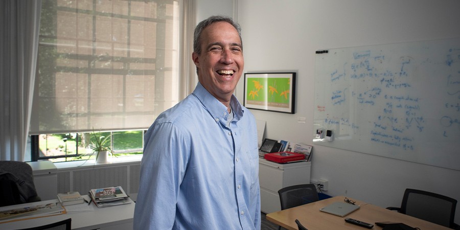 dan huttenlocher standing in his office wearing a blue shirt and smiling