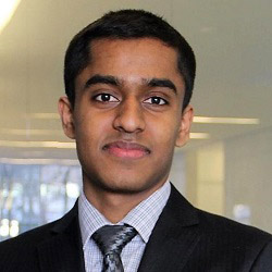 Mayuran standing in hall wearing a dark suit and grey pattern shirt