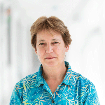 frances ross standing in bright white hallway wearing blue and green leaf print shirt