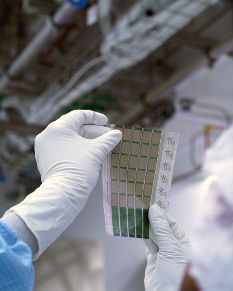 Gloved hands hold a sheet containing 6x5 grid of solar cells.