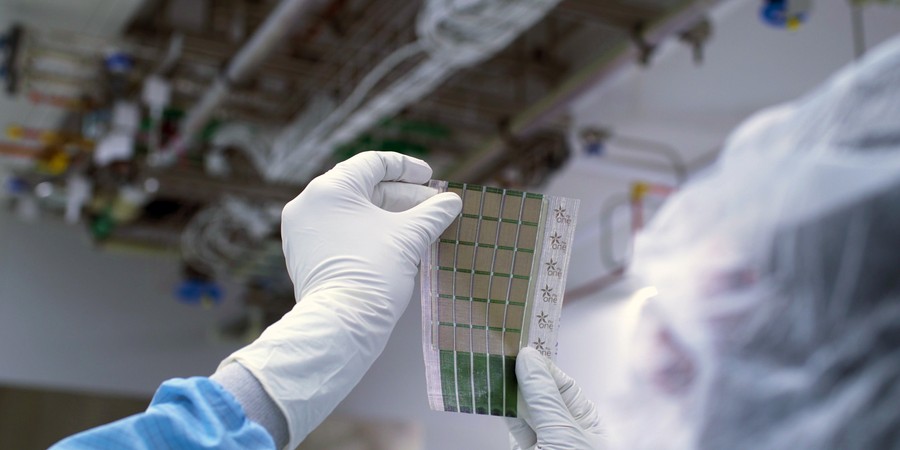 Gloved hands hold a sheet containing 6x5 grid of solar cells.