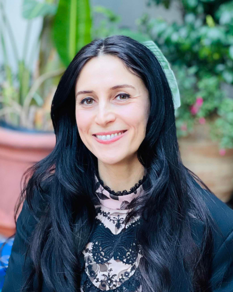 manya ghobadi with her hair down seated on a blue bench in a garden