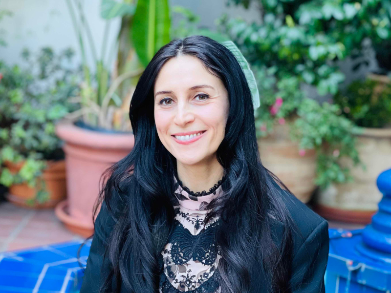 manya ghobadi with her hair down seated on a blue bench in a garden