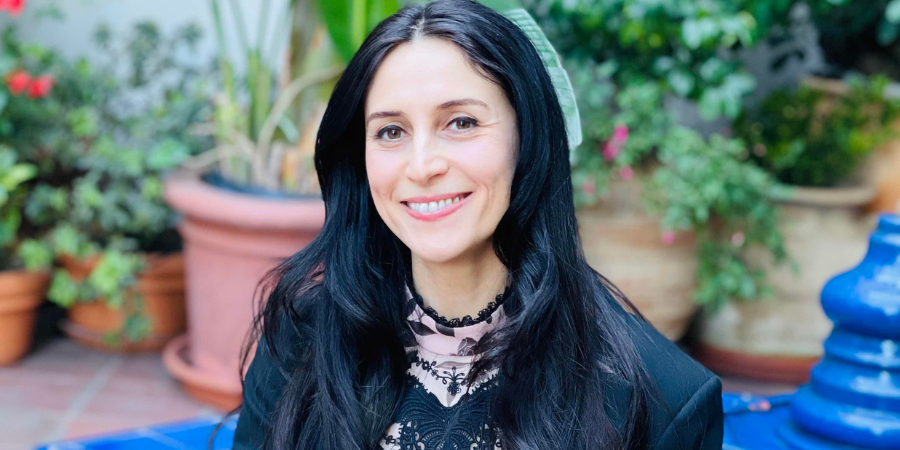 manya ghobadi with her hair down seated on a blue bench in a garden
