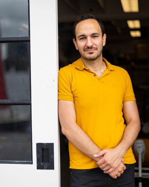 Fadel Adib stands between 2 glass panel sliding doors while wearing a yellow shirt and black pants.