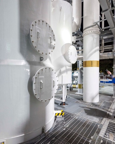 factory scientist wearing hard hat inspecting large white machines using flashlight
