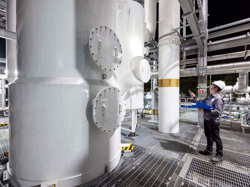 factory scientist wearing hard hat inspecting large white machines using flashlight