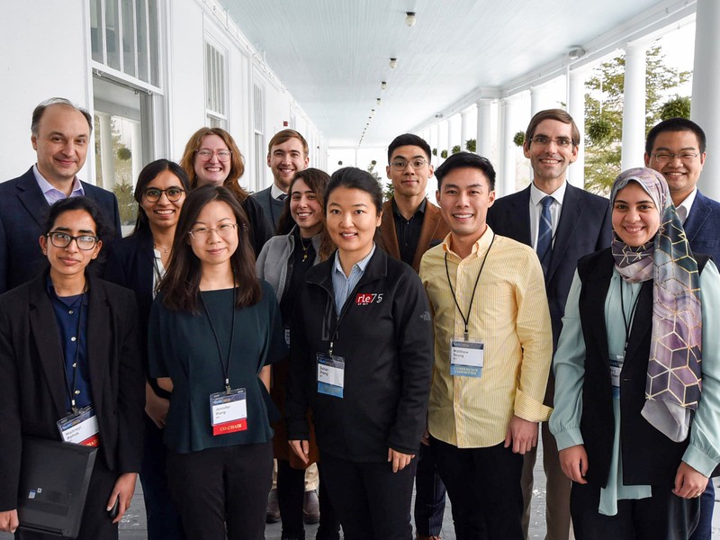 13 people in business attire pose for a group photo on a large, white covered porch