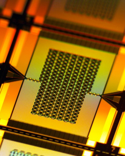 A yellow-lit closeup zooms in on one tiny, rectangular amplifier on the wafer. It has a chain-like rectangular grid in center that connects to the left and right edges of the wafer.