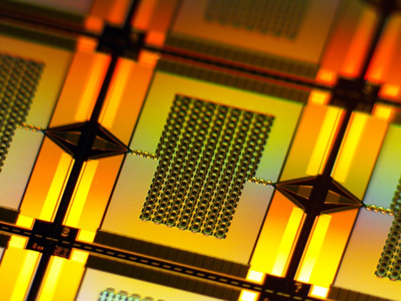 A yellow-lit closeup zooms in on one tiny, rectangular amplifier on the wafer. It has a chain-like rectangular grid in center that connects to the left and right edges of the wafer.