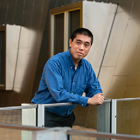julian shun in blue shirt leaning on metal railing outside grey metal building