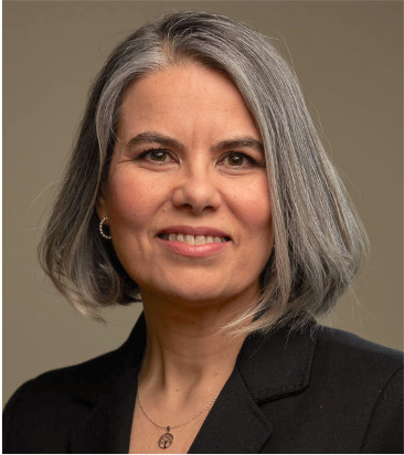 woman with grey hair wearing dark suit jacket in front of dark beige background