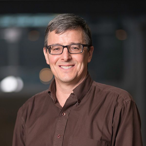 male with brown hair wearing black glasses and coffee brown button up shirt