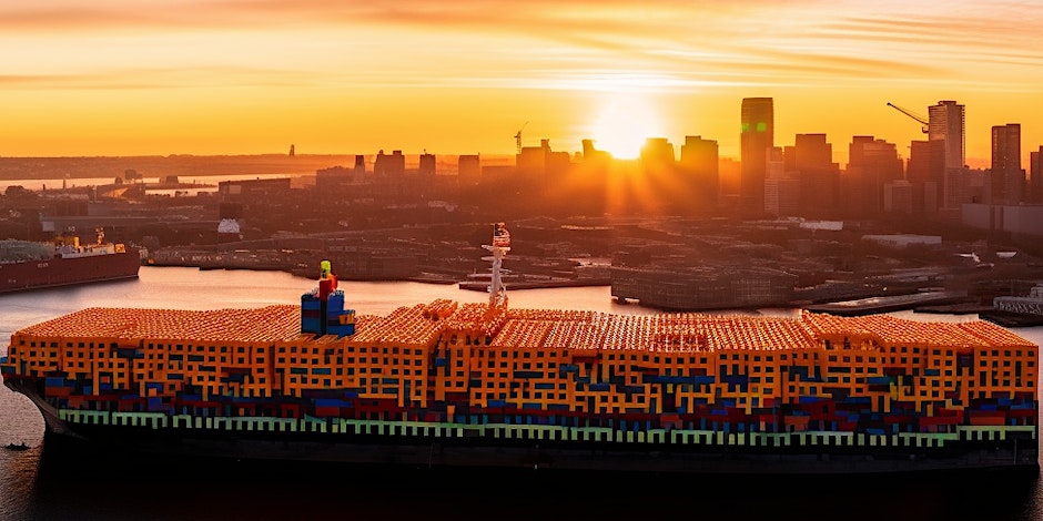 large container ship with stacks of hundreds of orange shipping containers docking into city port at sunset