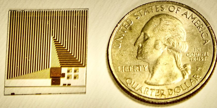 computer chip in shades of gold and brown laying next to a quarter coin for size comparison