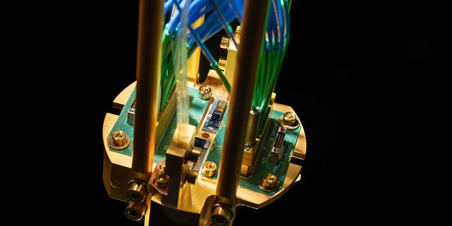 Close-up photo of a quantum repeater module mounted on a gold-plated copper assembly and connected to green printed circuit boards, with optical fibers routed up.