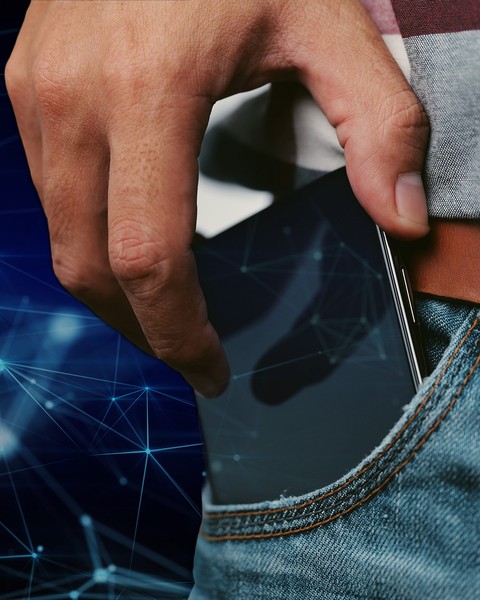 A cell phone peeks out from the pocket of a person wearing jeans, a belt, and a plaid shirt. In the background and on the cell phone’s screen are stylized connected nodes representing a neural network.