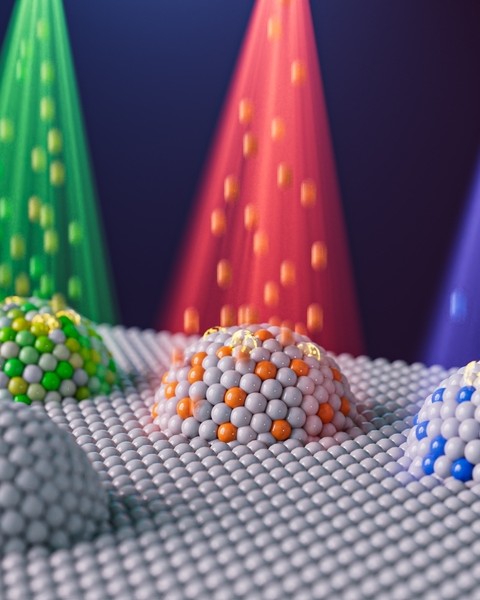 Artist’s concept of four domes comprised of spheres representing nanoparticles. Three of the domes have different colored particle beams shining down on them.