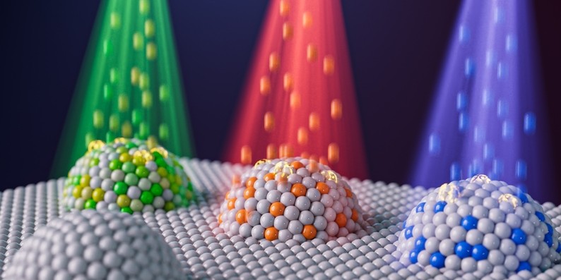 Artist’s concept of four domes comprised of spheres representing nanoparticles. Three of the domes have different colored particle beams shining down on them.