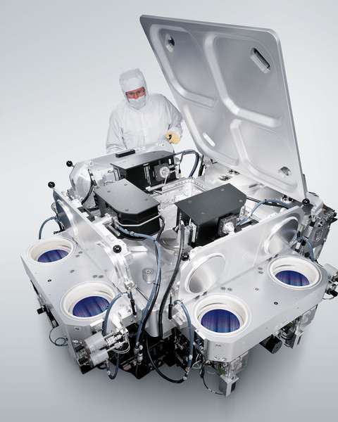 In this rendering, a person wearing head-to-toe PPE, including hood, gloves, and coveralls, works with a large assembly of nanofabrication equipment against a white background.