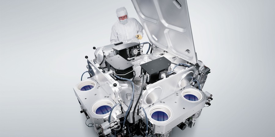In this rendering, a person wearing head-to-toe PPE, including hood, gloves, and coveralls, works with a large assembly of nanofabrication equipment against a white background.