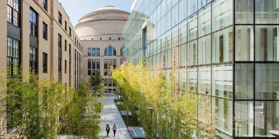 Exterior photo of the all-glass MIT.nano, at right; the brick Main Group building, at left; and a courtyard pathway down the middle, with MIT Dome in the background
