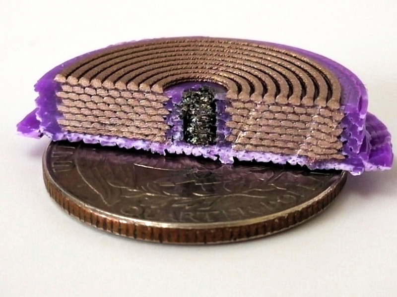 On top of a quarter sits a disc-like device chopped in half to show the interior: purple plastic is on outside, eight stacks of coiled copper-colored rods; and in the middle is a black substance.