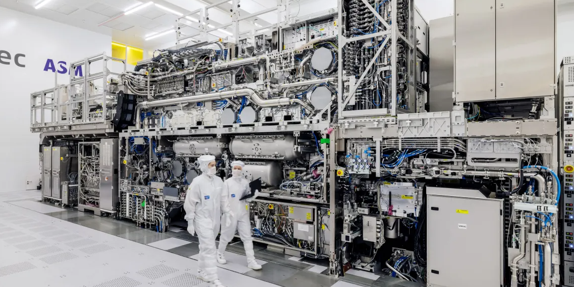 two workers entirely covered in white PPE walk through a factory next to large metal equipment