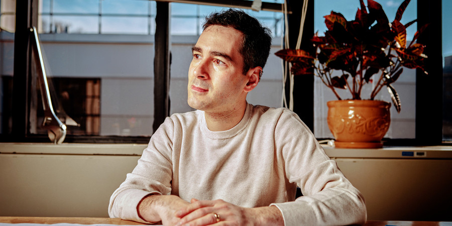 Rafael Jaramillo sits in his office and looks to the side. A large wrench sits on the window sill. The desk is covered in white paper with many drawings and notes on it.