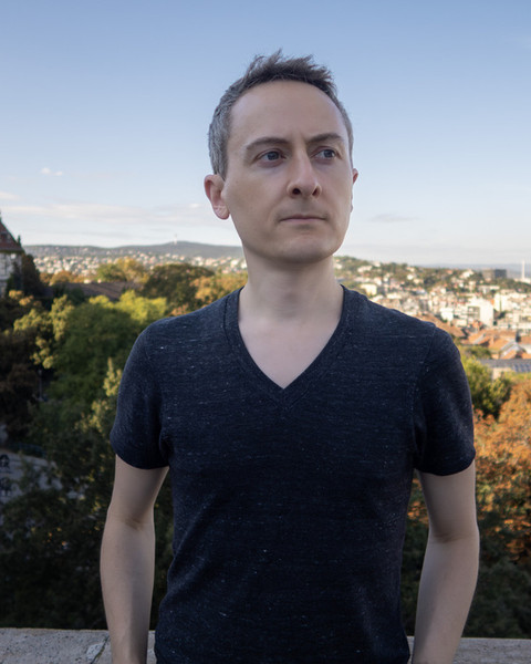 Jonathan Ragan-Kelley stands outdoors in Budapest, with the city as a backdrop