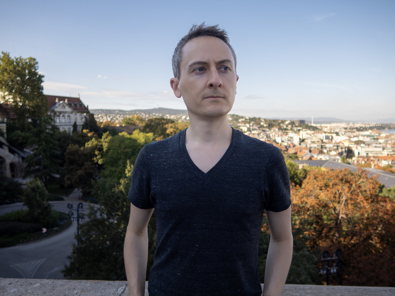 Jonathan Ragan-Kelley stands outdoors in Budapest, with the city as a backdrop