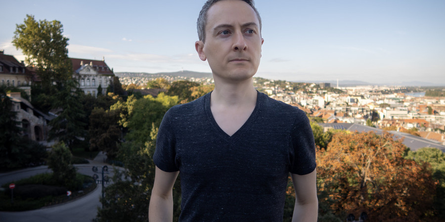 Jonathan Ragan-Kelley stands outdoors in Budapest, with the city as a backdrop