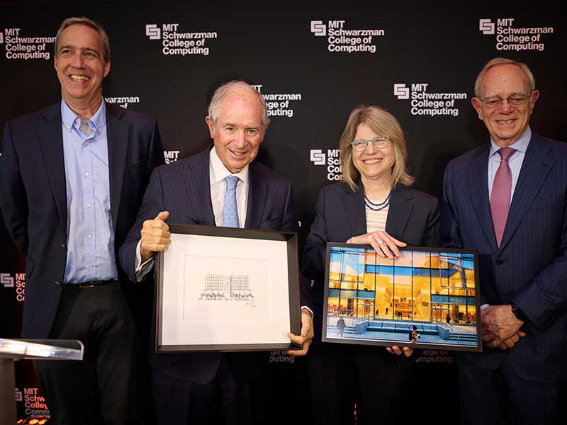 Dan Huttenlocher, Stephen Schwarzman, Sally Kornbluth, and L. Rafael Reif stand against a backdrop featuring the MIT Schwarzman College of Computing logo. Kornbluth holds a framed photo of a glass building, while Schwarzman holds a framed pencil drawing of the same building.