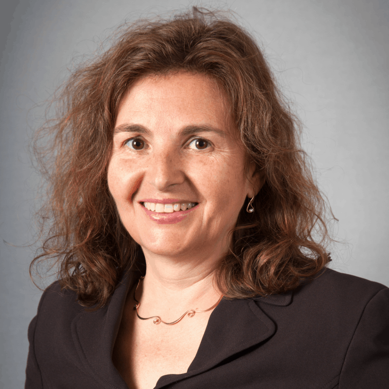 headshot of Daniela Rus wearing black suit jacket on a light grey backdrop