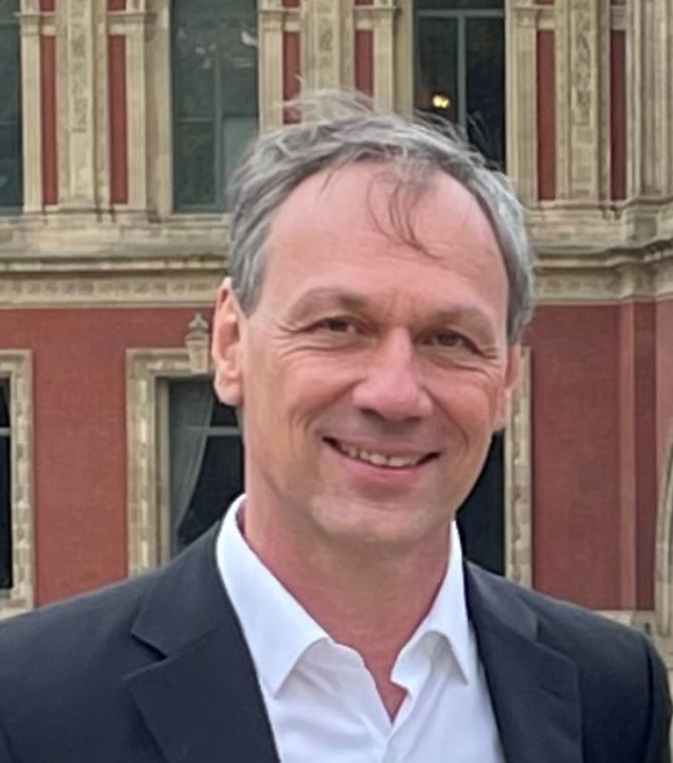 male wearing white dress shirt and black suit jacket in front of brick and stone building