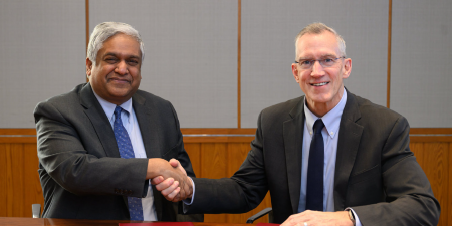 Anantha Chandrakasan and Gregg Bartlett, both in suits, sit at a table and shake hands for the camera