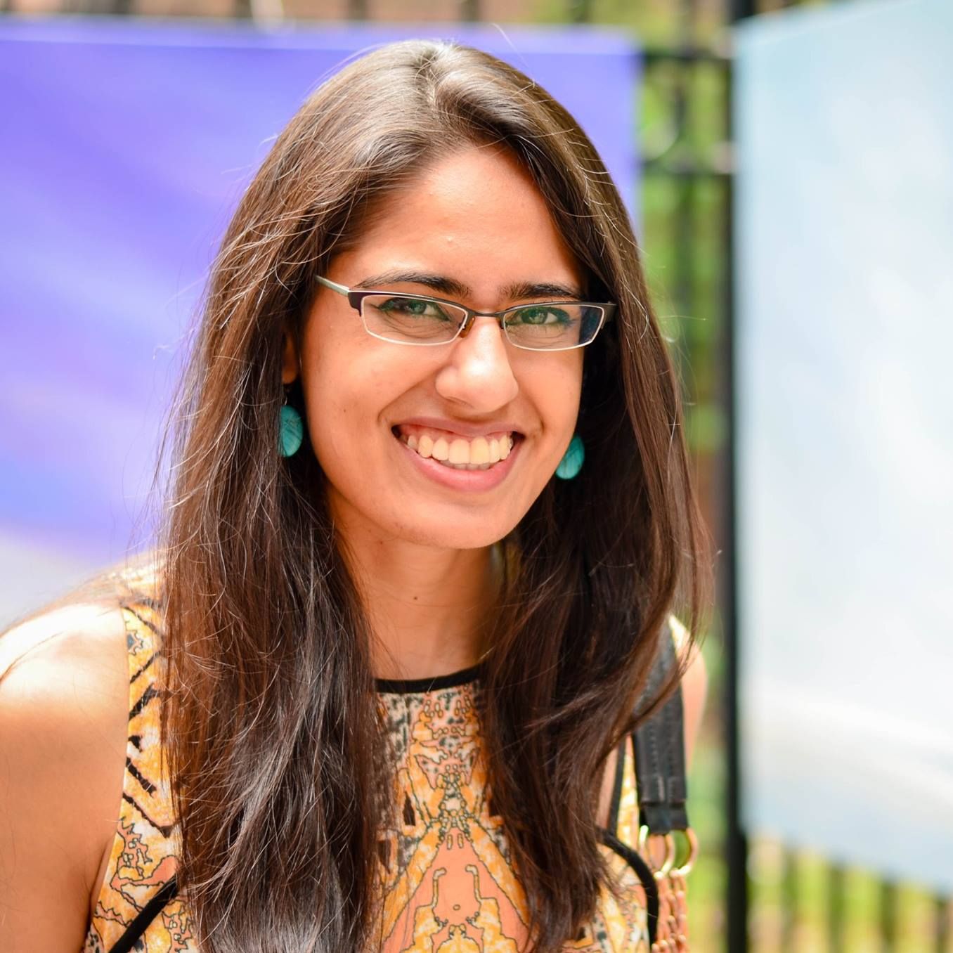 woman with long dark hair wearing a gold shirt in front of purple and green background