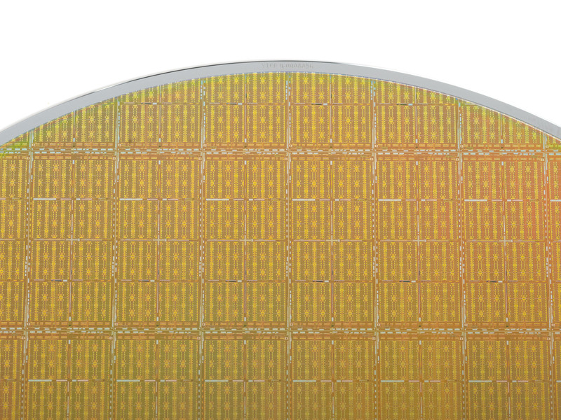 Close-up of a golden silicon disk against a white background. About 100 integrated circuits are visible within the disk.