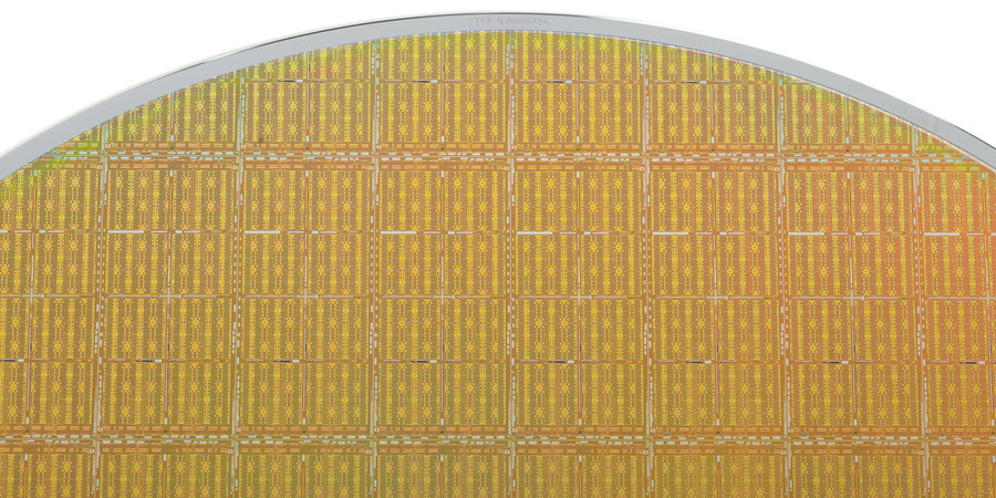 Close-up of a golden silicon disk against a white background. About 100 integrated circuits are visible within the disk.