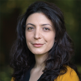 woman with dark hair wearing a black shirt and yellow sweater