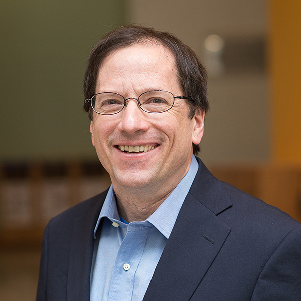 man with dark hair and glasses wearing blue suit
