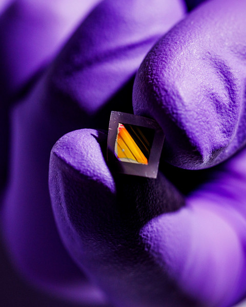 hand with purple medical gloves holding small diamond shape thin film material