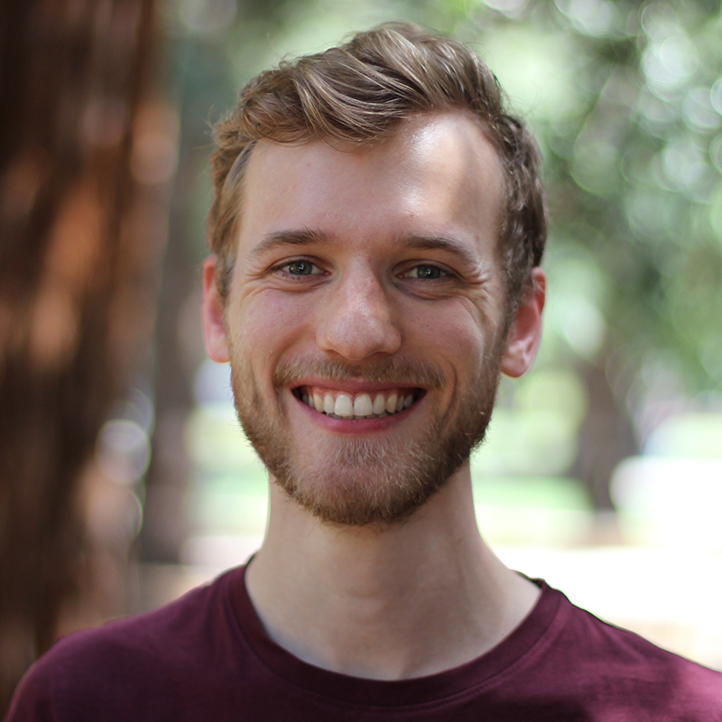 man wearing red shirt in front of blurred background of trees